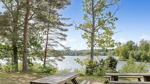 En picknickplats vid sjön med träbänkar och en grill.