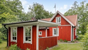 Ett rött trähus med en liten tillbyggnad, omgivet av grönska.