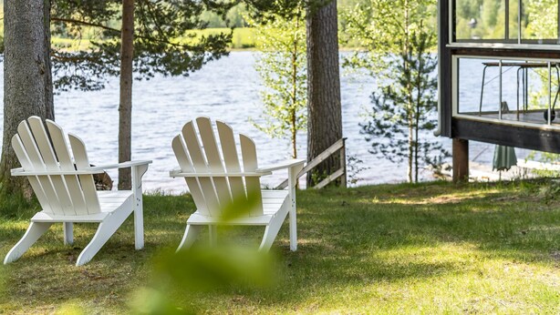 Deux fauteuils Adirondack sont placés face à un lac, avec une terrasse en bois et une véranda en verre.