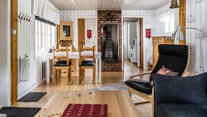 Une pièce chaleureuse avec un plancher en bois, un canapé noir, une table à manger avec des chaises, une cheminée et un coin cuisine visible à travers une porte ouverte.