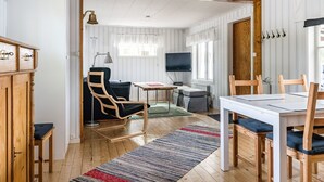Une pièce chaleureuse avec un plancher en bois, une table à manger avec des chaises, un téléviseur et une fenêtre avec des rideaux.