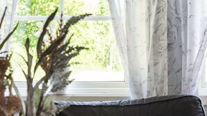 A room with a window, sheer curtains, a dark sofa, and a vase with dried plants. - Skärvudde Huset by Interhome (Kalvsvik)