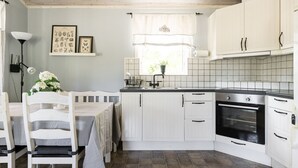 A kitchen with white cabinets, a black stove, and a window with curtains. - Skärvudde Huset by Interhome (Kalvsvik)