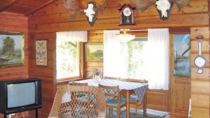 A rustic cabin interior with a dining area, wooden walls, a television, and various wall decorations including antlers and clocks. - Borrsjön by Interhome (Gräsmark)
