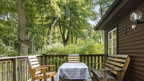 A wooden deck with a table and two chairs, surrounded by a wooden railing, overlooking a forested area.