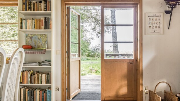 A cozy room with a wooden door leading to a garden, a bookshelf filled with books, and a wicker basket.