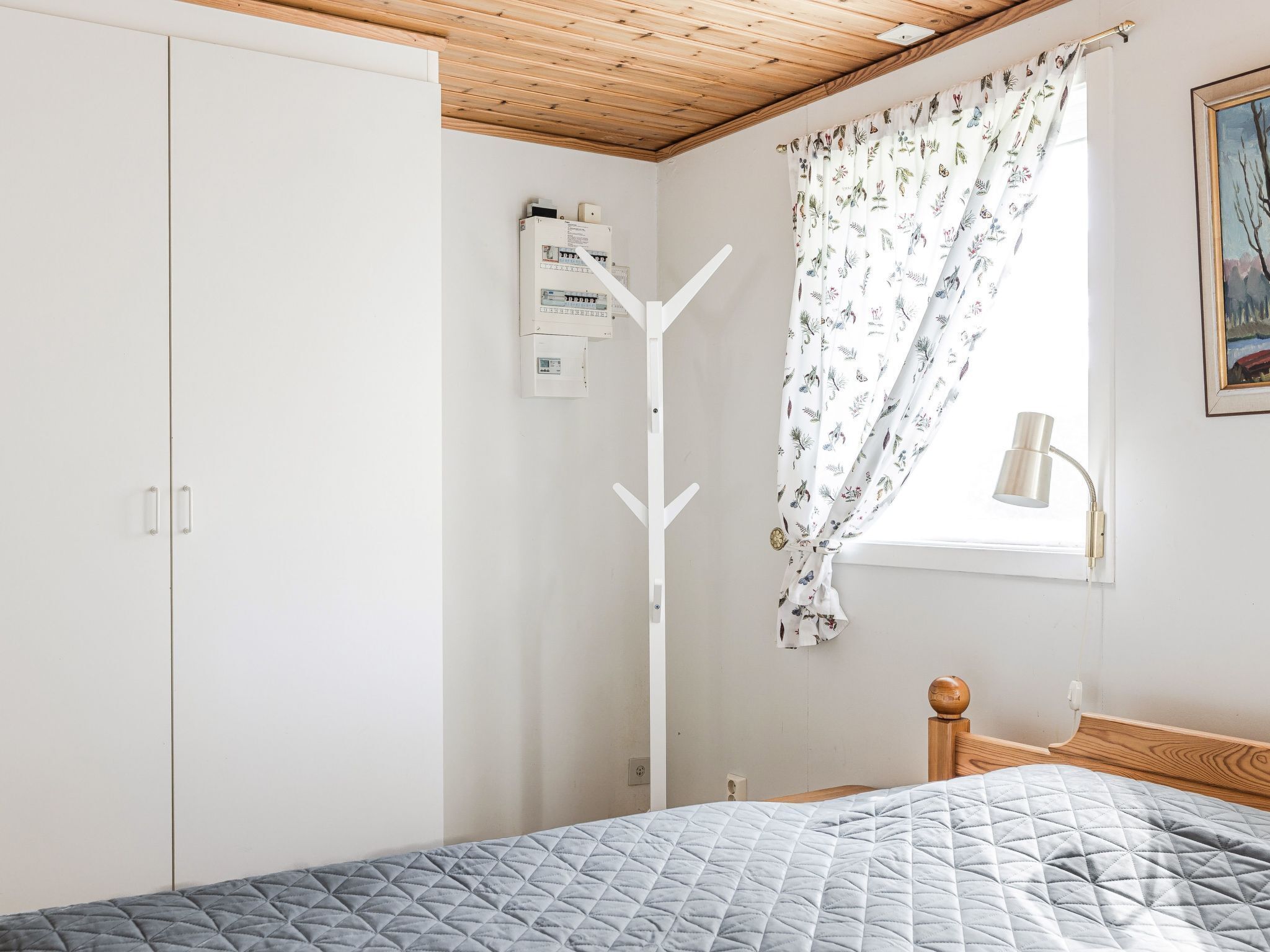A bedroom with a bed, a wardrobe, a window with curtains, a bedside lamp, and a ceiling light fixture.