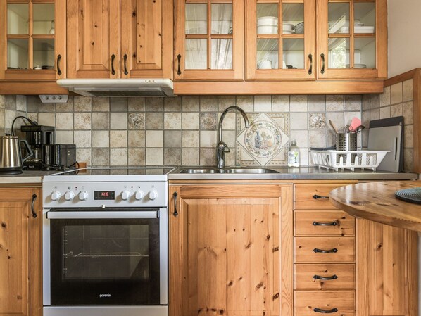 A kitchen with wooden cabinets, a stainless steel sink, a stove, and a tiled backsplash. - Kjuge Nya Huset by Interhome (Fjälkinge)
