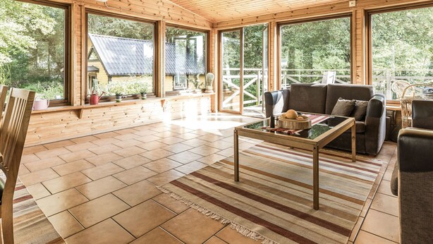 Un intérieur spacieux en bois, doté de grandes fenêtres, d’un canapé et d’une table basse.
