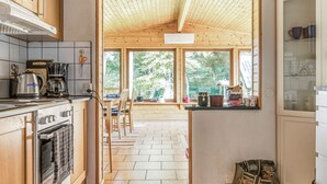 Une cuisine avec des meubles en bois, une cuisinière et une fenêtre donnant sur un coin repas équipé de chaises et d’une table.