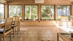 Un intérieur spacieux en bois, doté de grandes fenêtres, d’un coin repas avec des chaises et une table.