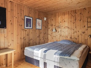 Una stanza con rivestimenti in legno, un letto, un tavolino e due quadri appesi al muro.