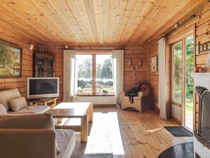 Interno di una baita di legno con televisione, divano e finestra vista alberi.