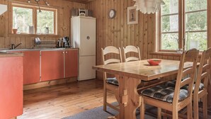 A wooden cabin interior with a kitchen, dining area, and large windows.