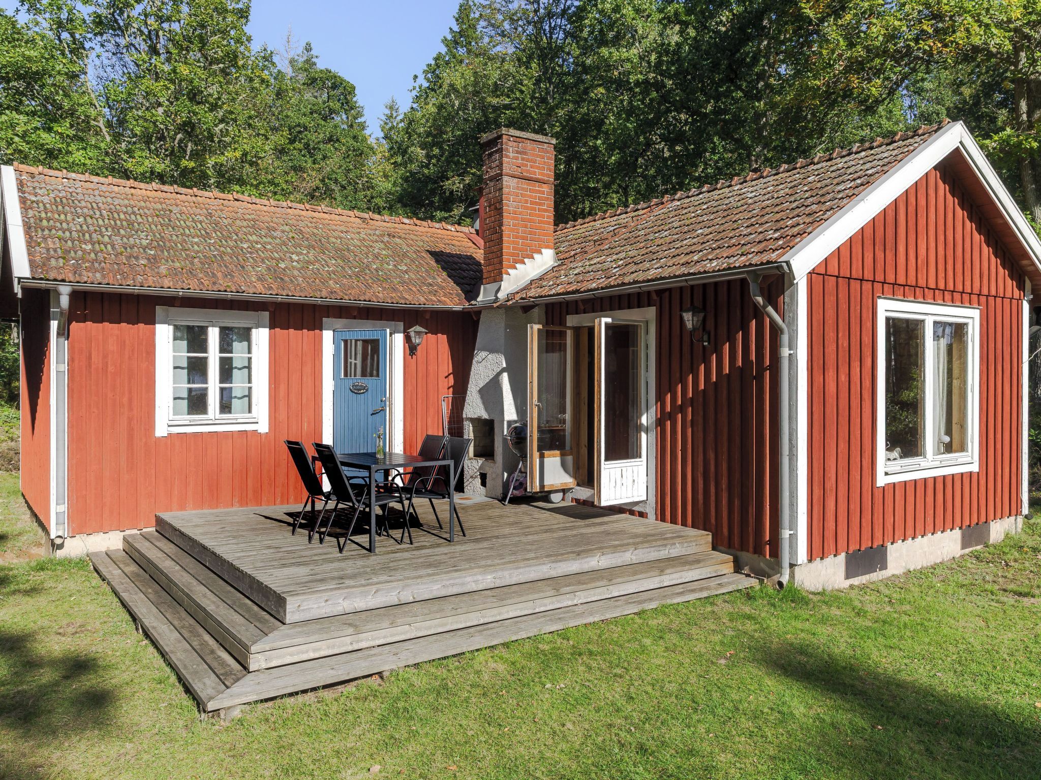A red wooden building with a tiled roof, a blue door, and a wooden deck with chairs.