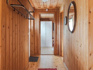 A wooden hallway with a door at the end, a small rug on the floor, and a circular mirror on the wall.