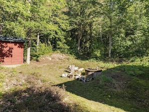 Une cabane en bois rouge, située dans une zone boisée, avec une pile de bûches et une structure en béton à proximité.