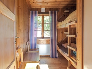 L’intérieur d’une cabane en bois, avec un lit superposé, un banc et une fenêtre avec des rideaux.