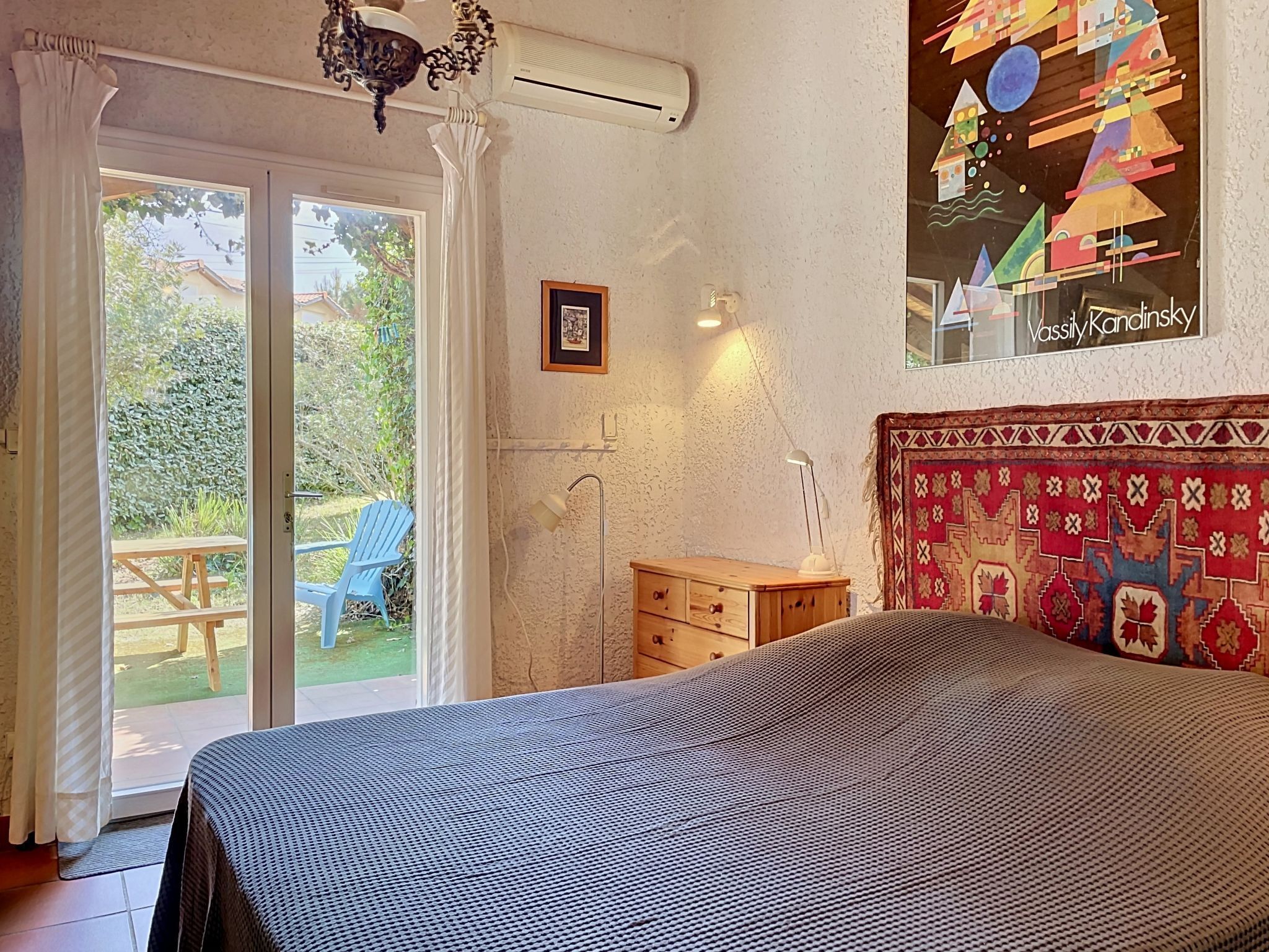 A bedroom with a bed, a window with curtains, a wooden dresser, and a wall with a patterned tapestry.