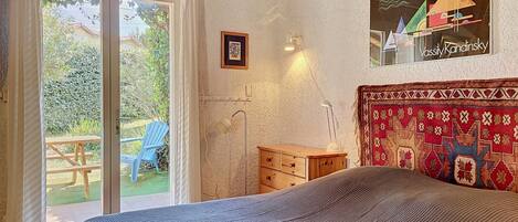 A bedroom with a bed, a window with curtains, a wooden dresser, and a wall with a patterned tapestry.