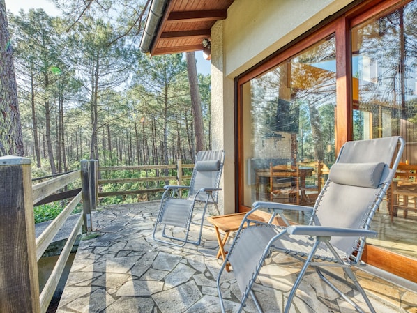 A stone-tiled patio with two metal chairs and a wooden table, overlooking a forested area. - Le Hameau du Point du Jour by Interhome (Lacanau)