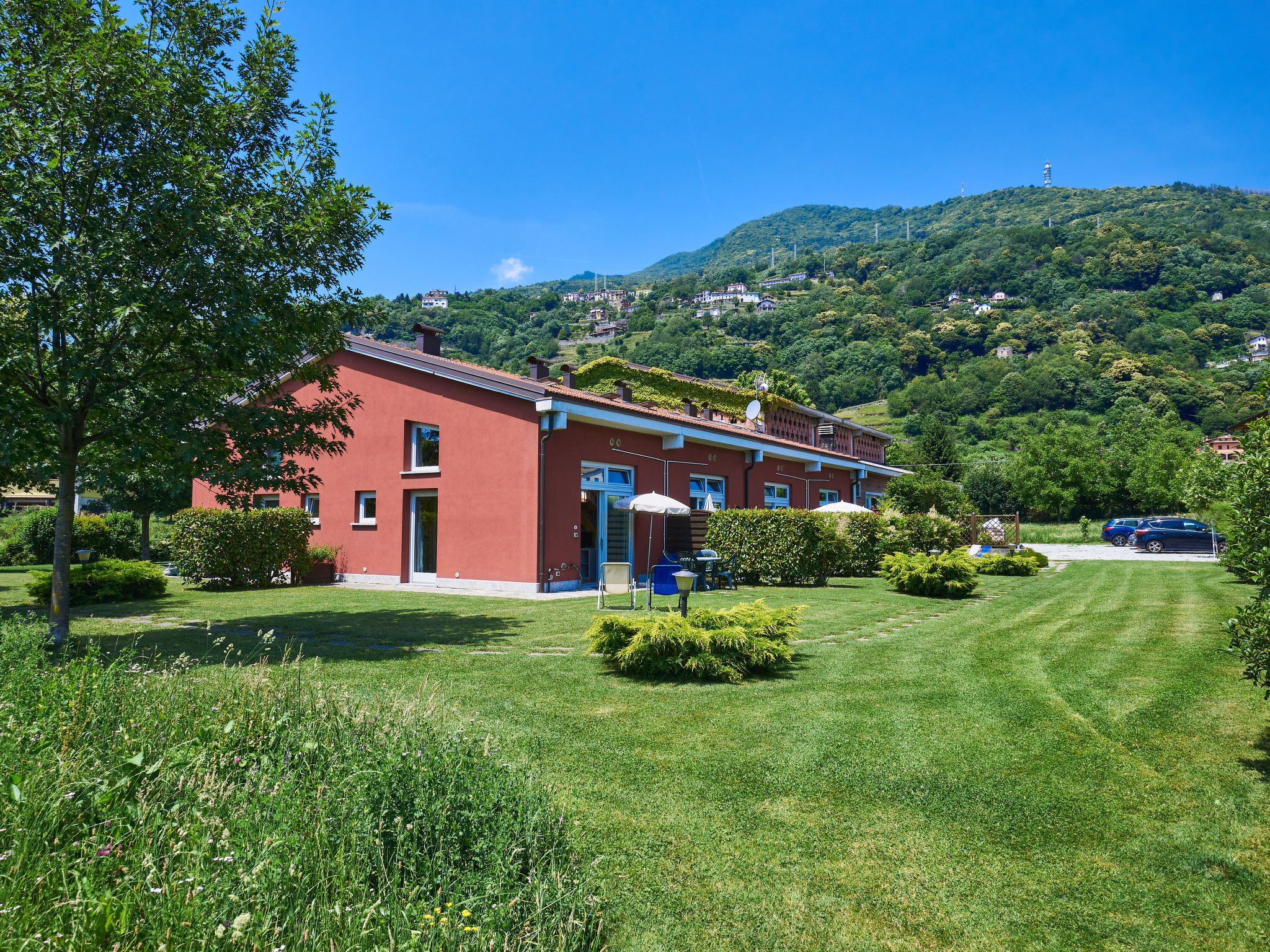 A red building with a garden in front, surrounded by greenery and hills.