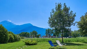 A grassy area with two lawn chairs and a tree, with mountains in the background. - Gelsomino by Interhome (Dongo)