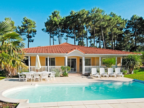A house with a swimming pool, white outdoor furniture, and a red-tiled roof.