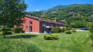 A red building with a garden in front, surrounded by greenery and hills. - Gelsomino by Interhome (Dongo)