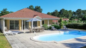 A house with a swimming pool, a covered patio with chairs and an umbrella, and a garden. - Eden Parc Golf de l'Ardilouse V8I by Interhome (Lacanau)