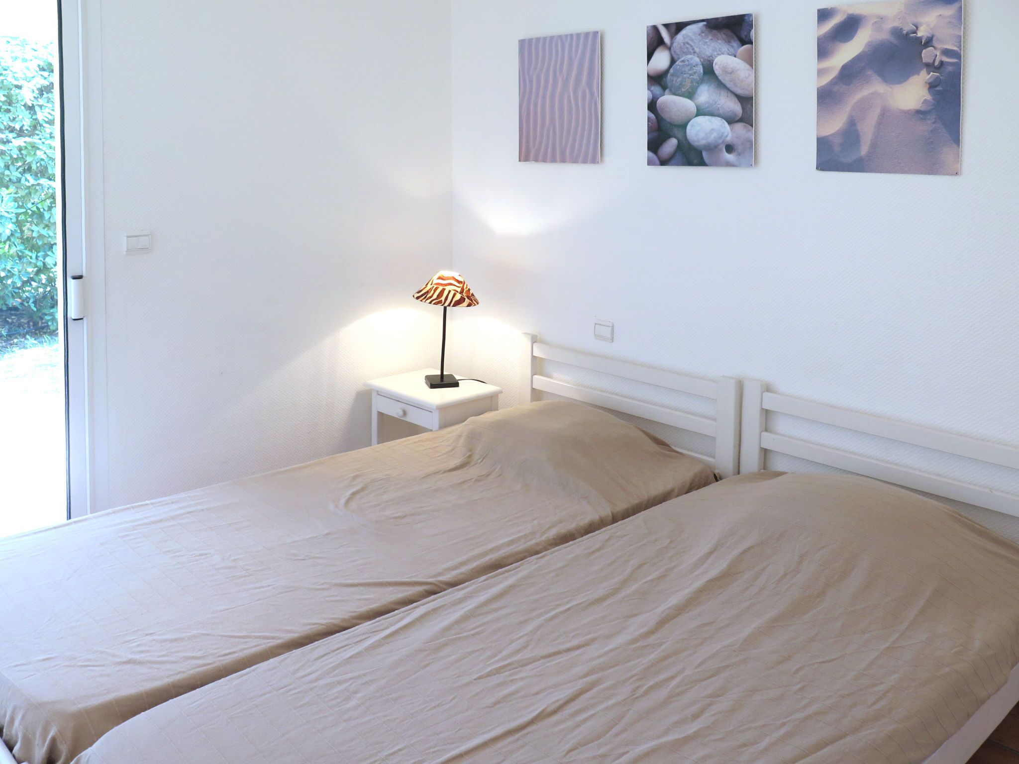 A bedroom with two beds, a nightstand with a lamp, and two wall art pieces.