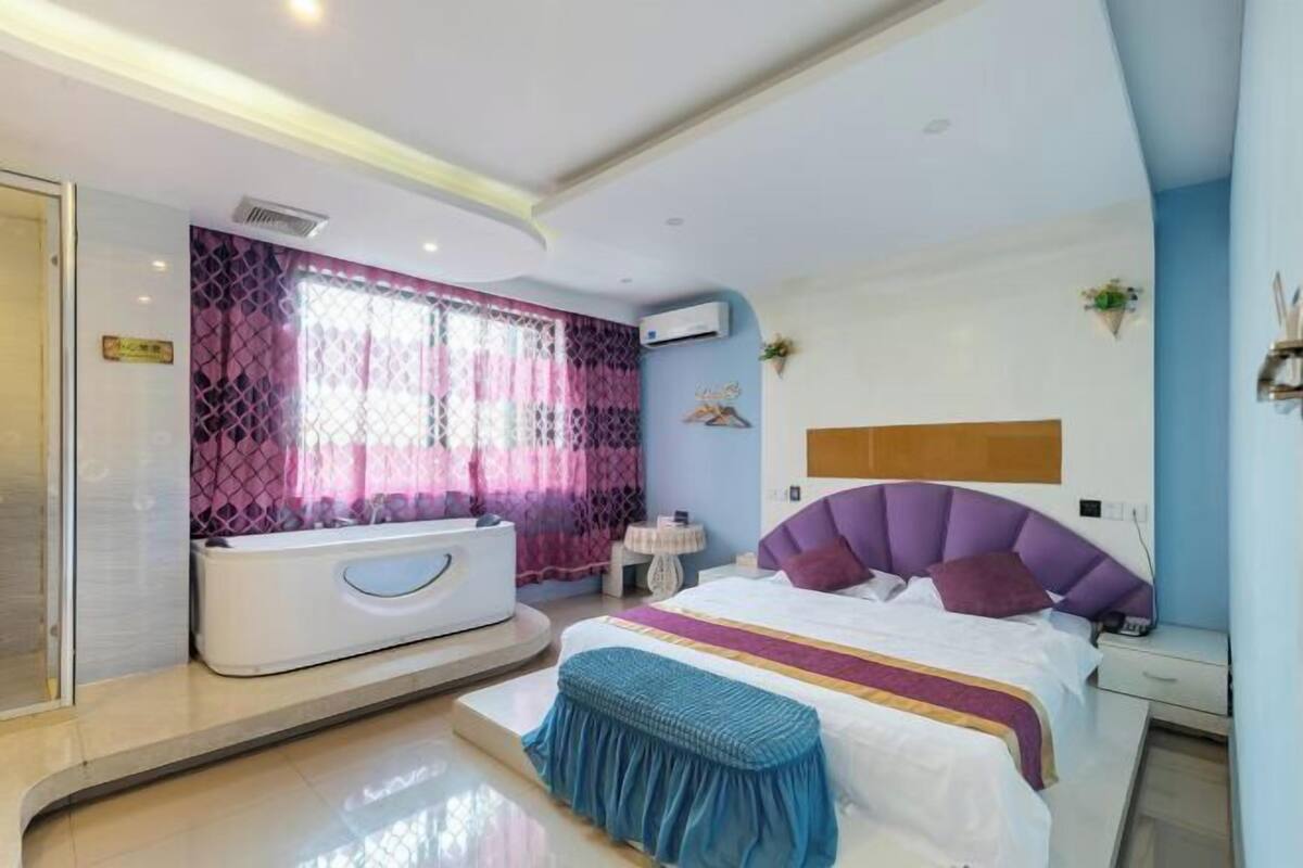 A modern bedroom with a large bed, a built-in bathtub, and a small bedside table.