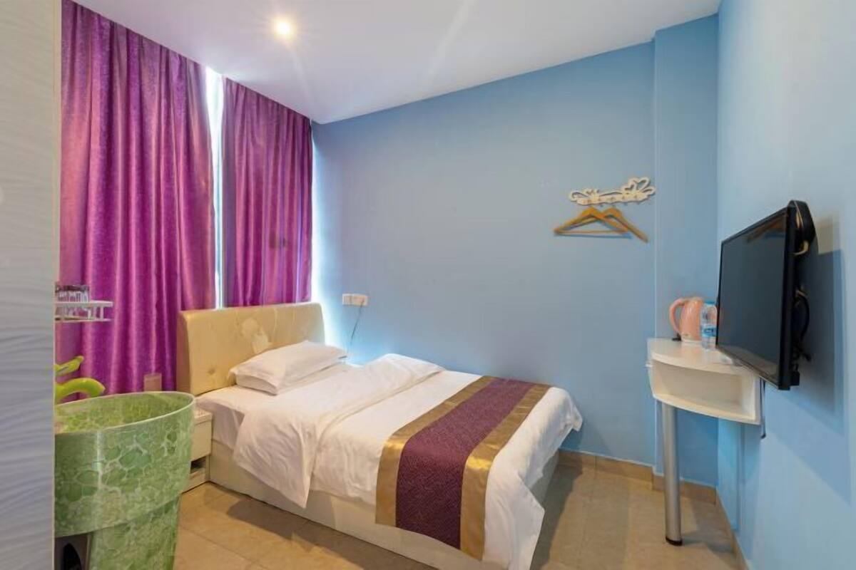 A hotel room with a bed, a television, a sink, and a window with curtains.