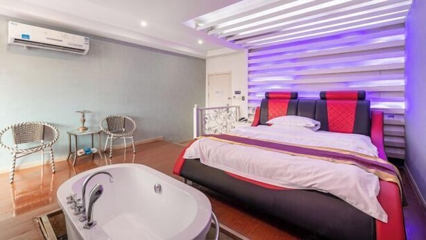 A modern hotel room with a large bed, a separate bathroom with a bathtub, and a seating area with two chairs. - Light Stay·Noli Theme Hotel (Shanghai Fengxian Nanqiao Branch) (Shanghai)
