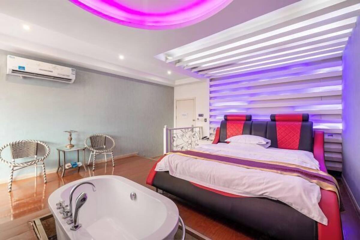 A modern hotel room with a large bed, a separate bathroom with a bathtub, and a seating area with two chairs.