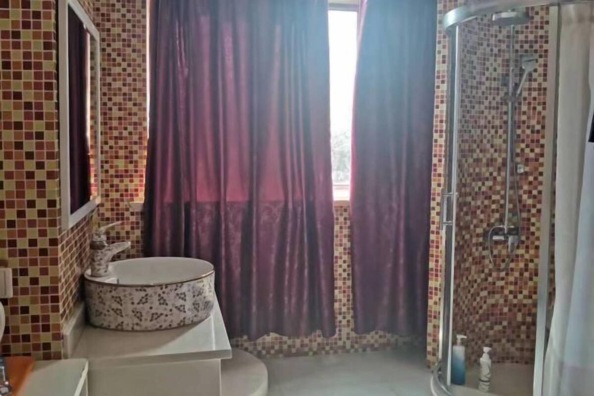 A bathroom with a tiled wall, a round sink, a shower, and purple curtains.