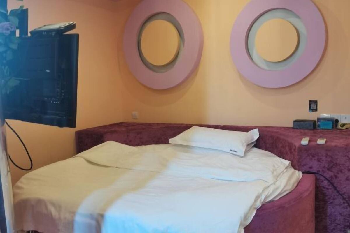 A hotel room with a bed, two circular wall decorations, a flat-screen TV, and a bedside table with a lamp.