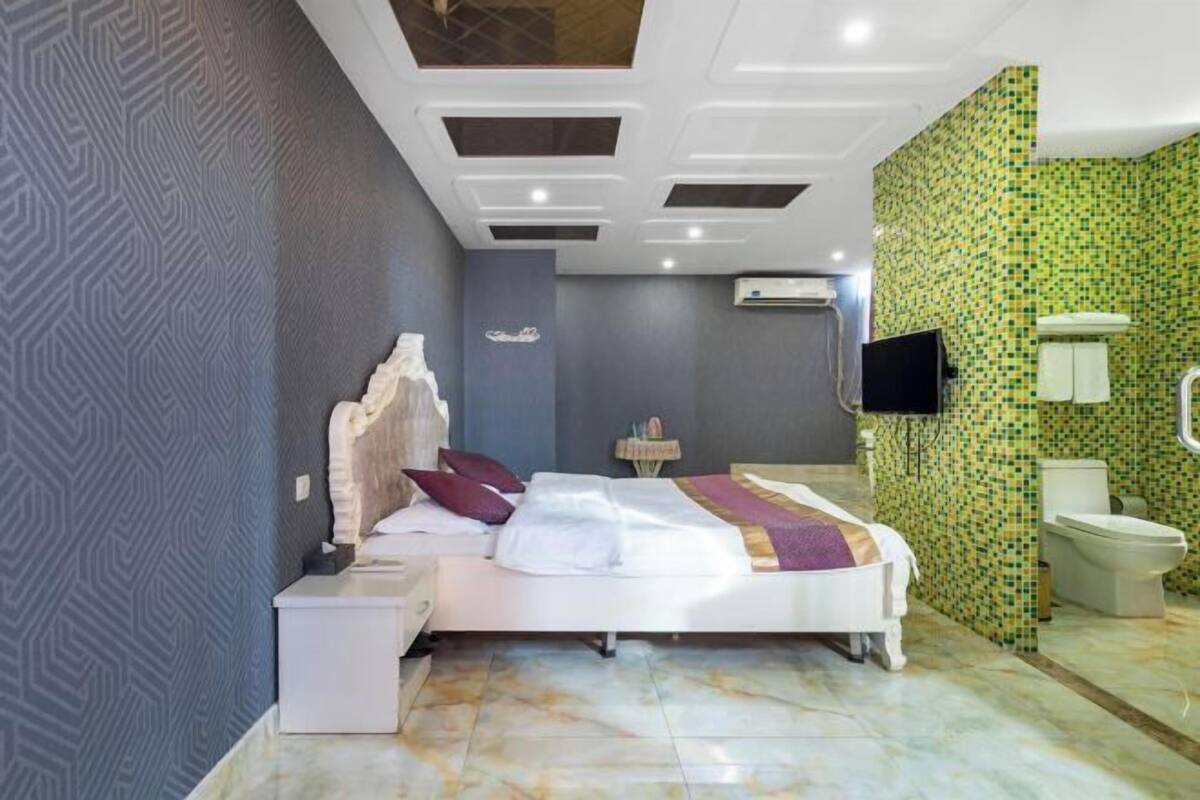 A hotel room with a bed, a nightstand, a TV, a bathroom with a toilet, and a shower.