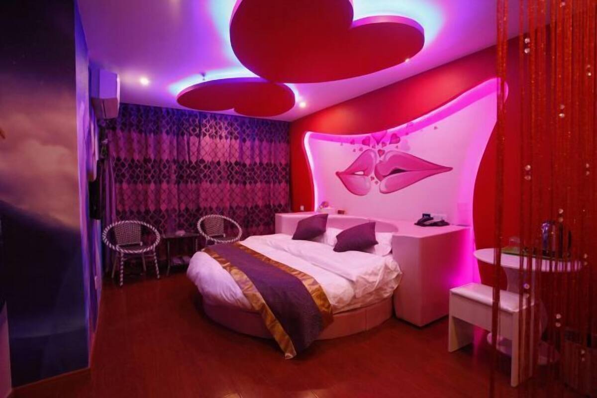 A modern bedroom with a curved wall, a bed, a nightstand, a chair, and a mirror.