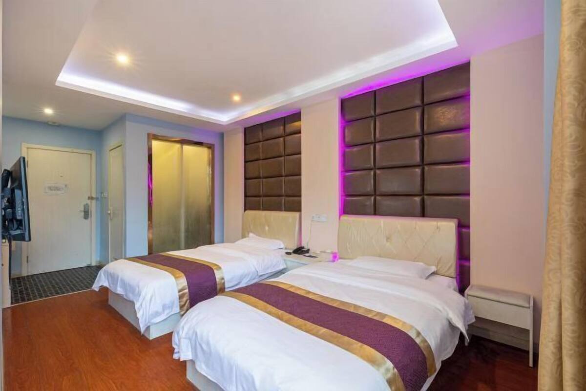 A hotel room with two beds, a headboard with a padded design, a ceiling with recessed lighting, and a visible door.