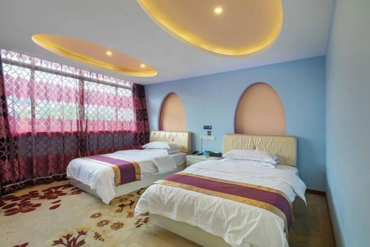 A hotel room with two beds, a patterned carpet, and a window with patterned curtains.