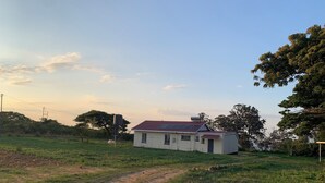 A small house with a red roof and solar panels, surrounded by a grassy field and trees.