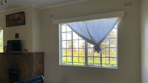 A room with a stone fireplace, a bench, a television on a stand, and a window with a curtain.