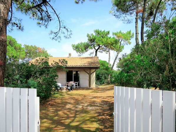 A small house with a tiled roof, a patio with chairs, and a white fence in front.