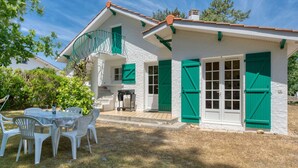 Una casa blanca con contraventanas verdes, un balcón y un patio con sillas y una mesa de plástico.