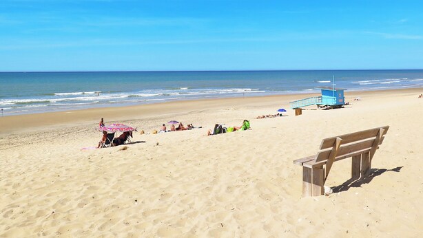 Una playa con una torre de salvavidas, un banco de madera y gente relajándose.