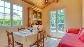 Un comedor con una mesa preparada para cuatro personas, sillas de madera y una cocina con armarios de vidrio.