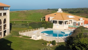 Um hotel com piscina, campo de golfe ao fundo e vista para o mar.