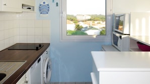 Uma cozinha compacta com máquina de lavar, micro-ondas e janela com vista para edifícios.