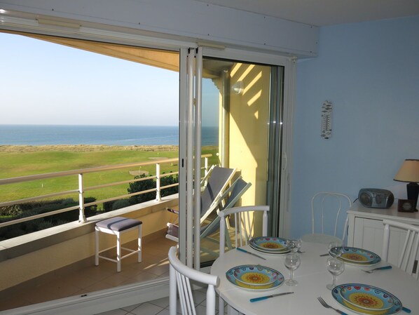 A balcony with a table set for two, overlooking a coastal landscape.